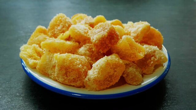 Closeup circular dolly shot of sugar coated, crystallised ginger pieces on a small plate.