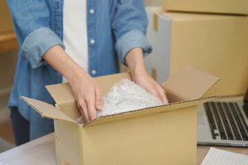 Small business entrepreneur SME, hand of woman owner packing product, putting parcel into the cardboard box after receive order from customer, working at home office. Merchant online, ecommerce.