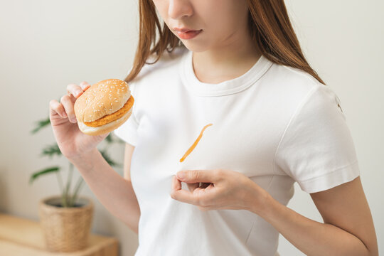 Cloth Stain, Disappointment Asian Young Woman, Girl Eat Food Hand Hold Hamburger, Burger Show Making Tomato Sauce Smudged Spilling, Drop On White T-shirt, Spot Dirty Or Smudge On Clothes, Dirt Stains.