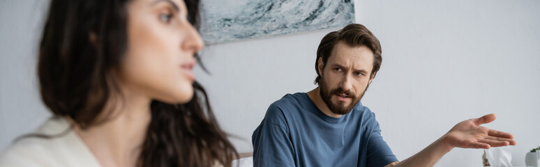 Offended man pointing with hand while talking to blurred girlfriend at home, banner.