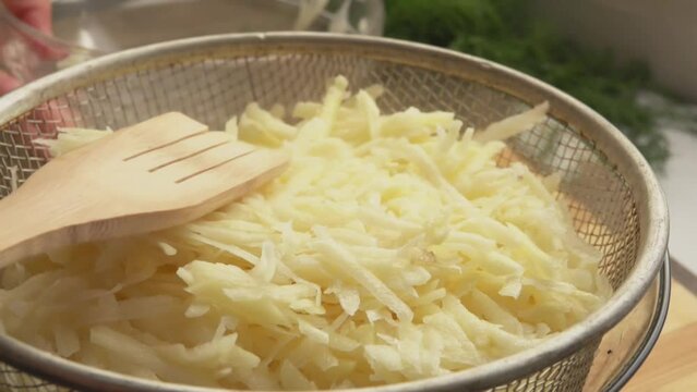 Close-up of the raw grated potato pressed to the colander with the spatula