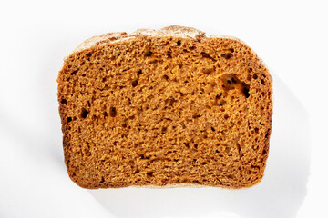 Slice of fresh delicious dark bread on white background in sunlight close up