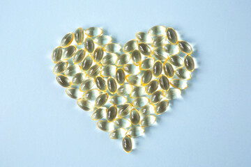 Transparent capsules with vitamin D or Omega-3 in the form of a heart is on a blue background. View...