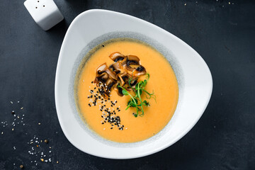 Fresh pumpkin cream soup with champignons, microgreens and sesame seeds.