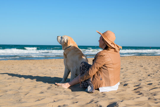 Woman with a hat and her dog enjoying sitting on the beach