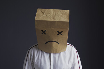 A man in a shirt with a bag on his head, with a sad smiley face drawn, is crying