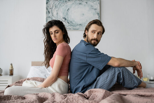 Upset woman in pajama sitting back to back with asexual boyfriend on bed.