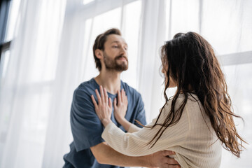 Woman pushing blurred aggressive boyfriend during quarrel at home.
