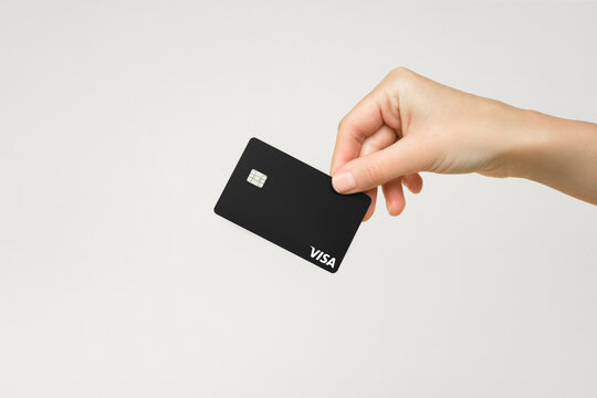 female hand holds a black plastic Visa card on a gray background
