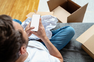 Mobile phone with blank screen in male hands, cardboards boxes on background.