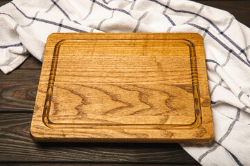 Cutting board over towel on wooden kitchen table. Cutting board and kitchen towel on brown textured background. Menu food card or recipes background concept.MOCKUP. Design. Place for text, copy space.