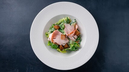 Salad with chicken ham, cucumber, lettuce, croutons and mayonnaise on a dark table.