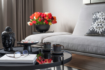 Modern home interior. Comfortable grey sofa, gorgeous flowers in a vase, covered coffee table with sweets and cups of coffee. Cozy home corner.