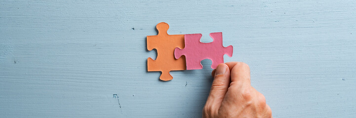 Wide view image of male hand joining two matching colorful puzzle pieces