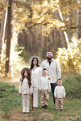 Portrait of big family outdoors. Young Stylish bearded dad with little son on shoulder, beautiful brunette mom, child boy and daughter in autumn park, smiling and looking at camera. Happy family day