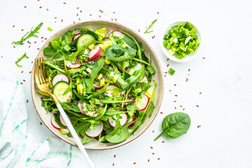 Obraz premium Green salad with spinach, arugula and radish with olive oil on white table. Top view with copy space.