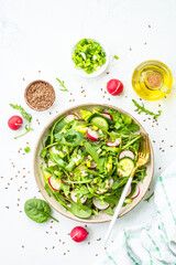 Green salad with spinach, arugula and radish with olive oil on white table. Top view with copy space.