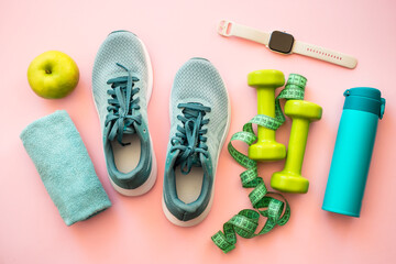 Fototapeta na wymiar Healthy lifestyle and fitness concept. Sneakers, dumbbells, towel, green apple and fitness bracelet. Flat lay on pink.