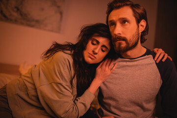 Brunette woman hugging sad boyfriend in bedroom at night.