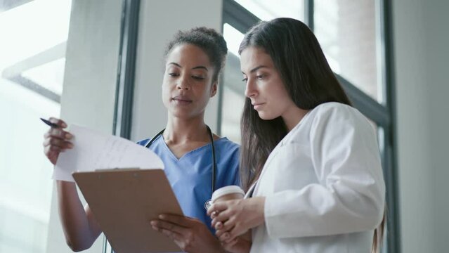 Video of  two beautiful young female doctors talking each other while holding folder with notes in the hospital.