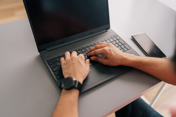 Close-up high-angle view of unrecognizable business man typing on laptop computer sitting at desk in light office room. Closeup cropped shot of freelancer blogger working on laptop at home office room