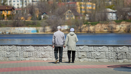 two elderly people are walking and holding hands