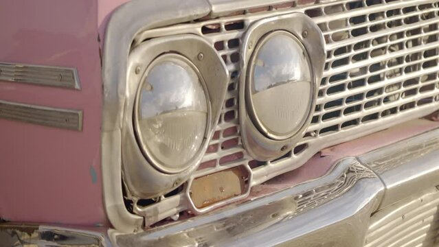 Close up of dusty turned off headlights of a pink retro car. Action. Stylish old fashioned car exterior.