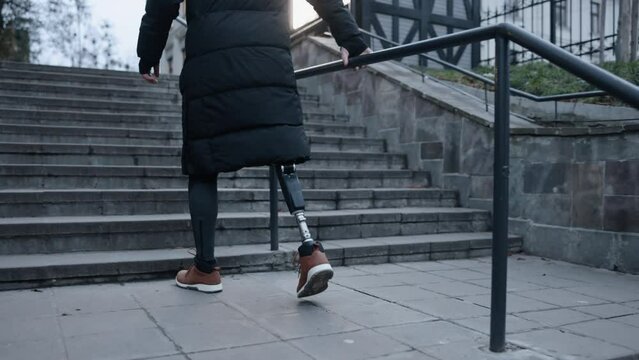 Disability climb, Climbing support, Artificial limb. Act of ascending stairs on city street performed by man who is disabled and has prosthetic leg.