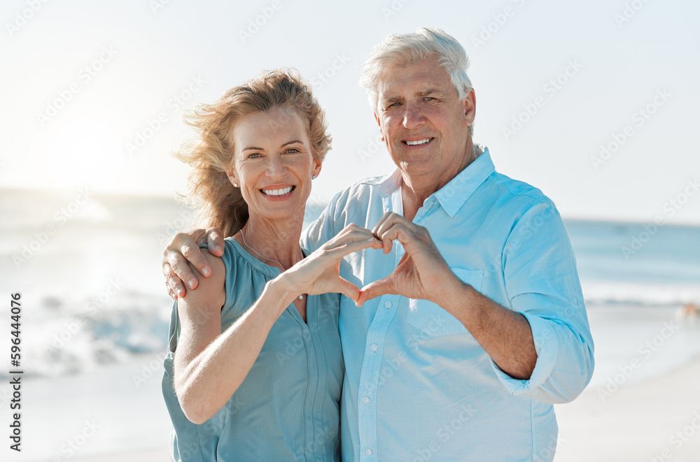 Sticker love conquers all things. shot of a mature couple forming a heart with their hands while at the beac