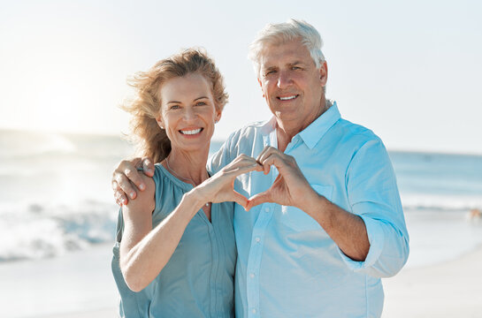 Love conquers all things. Shot of a mature couple forming a heart with their hands while at the beach. - Powered by Adobe