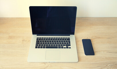 Laptop with blank black screen with smartphone on wooden table, workplace in interior room