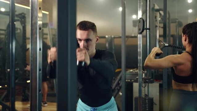 Medium shot of handsome man doing exercises on vertical row machine in gym. Back workout. Sports equipment, woman and man training in the background. andHigh quality 4k footage