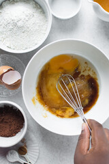 Whisking eggs and brown sugar in a white mixing bowl, baking process for madeleines