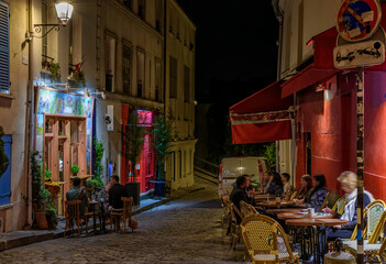 Night cozy street with tables of cafe in quarter Montmartre in Paris, France. Architecture and landmark of Paris. Paris cityscape.