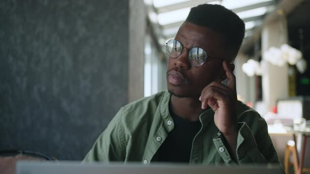 A thoughtful young African American startup founder is lost in thought while working on his laptop at a cafe, pondering creative solutions to business problems