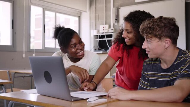 Group of three smiling multicultural teenage students looking at the laptop discussing the subject seminar in the high school classroom. Concept of education. Generation Z people.