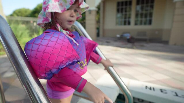 Little girl with floaties smiling at camera while trying to get into a swimming pool