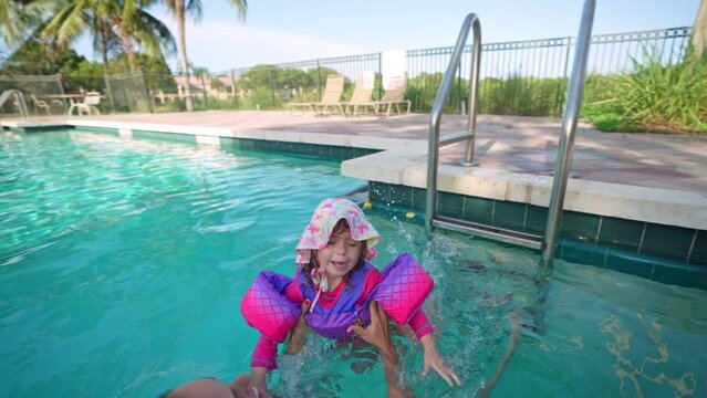 Beautiful little girl with floaties jumping to mom's arms in swimming pool