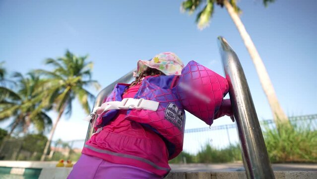 Little girl with floaties getting out of the pool through the stairs