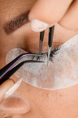 close-up top view on eyelash extension procedure. Master tweezers accurate attaches lashes