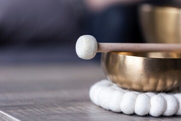 A close up of a tibetan singing bowl or himalayan bowl, with a mallet lying on top of it to make a relaxing sound. The object is used for meditation, relaxation and therapy to relieve stress.