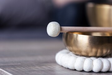 A portrait of a tibetan singing bowl or himalayan bowl, with a mallet lying on top of it to make a relaxing sound. The object is used for meditation, relaxation and therapy to relieve stress.