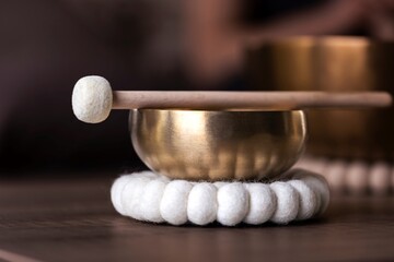 A portrait of a tibetan singing bowl or himalayan bowl, with a mallet lying on top of it to make a relaxing sound. The object is used for therapy to relieve stress and relaxation, meditation.