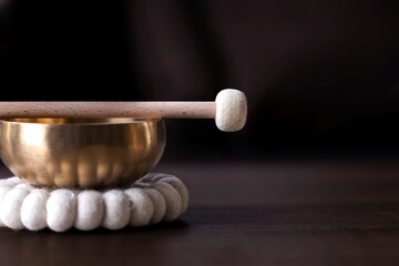 A close up portrait of half of a tibetan singing bowl with a mallet on it and negative space to the...