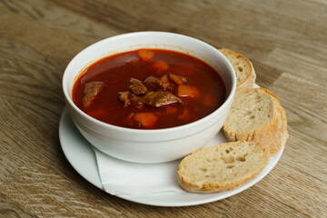 Traditional Hungarian Goulash Soup with Bread on a wooden table