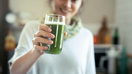 Young woman drinks a glass of green healthy smoothie