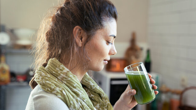 Young woman drinks a glass of green healthy smoothie