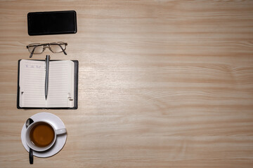 Desk with eyeglasses, notepad, smartphone, pen and a cup of tea on a wooden table. Top view with copy space. Flat lay - image