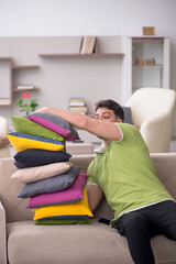 Obraz premium Young man with a lot of pillows sitting on the sofa