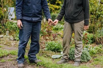 Elderly man and woman gardeners hold hands while standing outdoors in a garden in nature. Photography, the concept of eternal love.